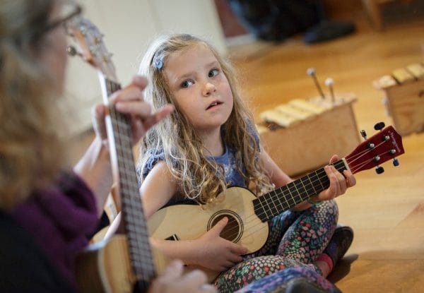 little girls sitting on the floor strumming the ukulele