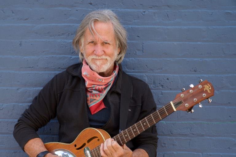 Man standing with guitar smiling.