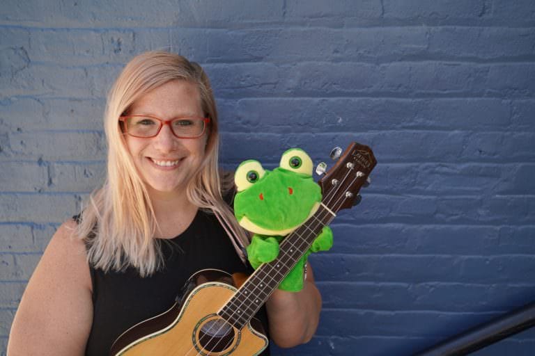 Woman smiling holding a ukulele and puppet