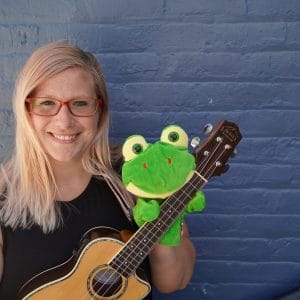 Woman smiling holding a ukulele and puppet