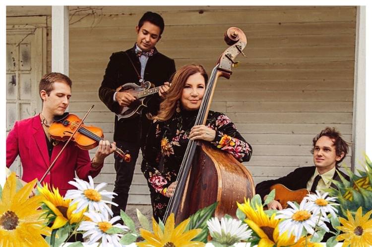 Missy Raines with 3 members of her band all holding instruments sitting and standing on a porch.