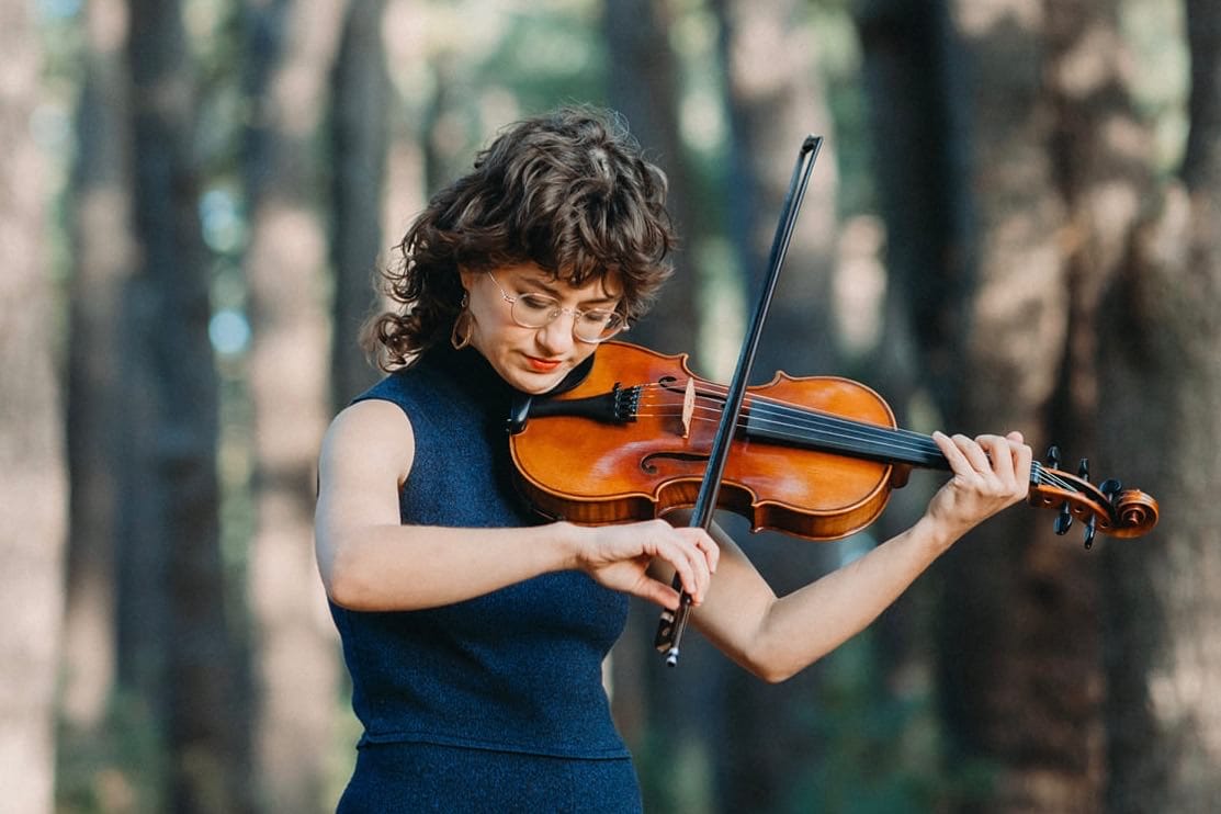 Image of Sophie Wellington playing violin, with trees in the background, blurred out.